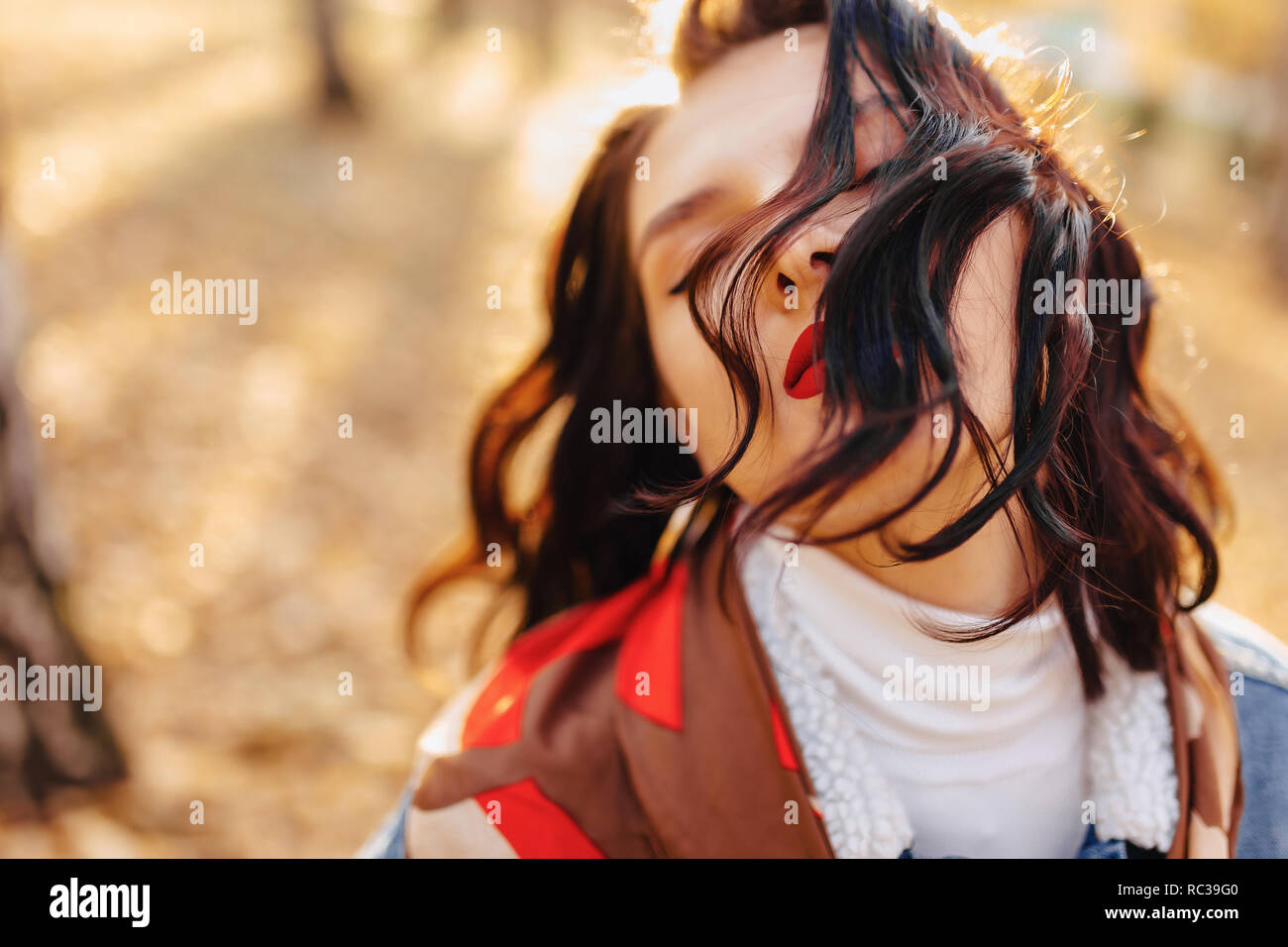 Joven chica bonita con labios rojos y pelo corto en un abrigo de mezclilla camina en la soleada ciudad de otoño Foto de stock