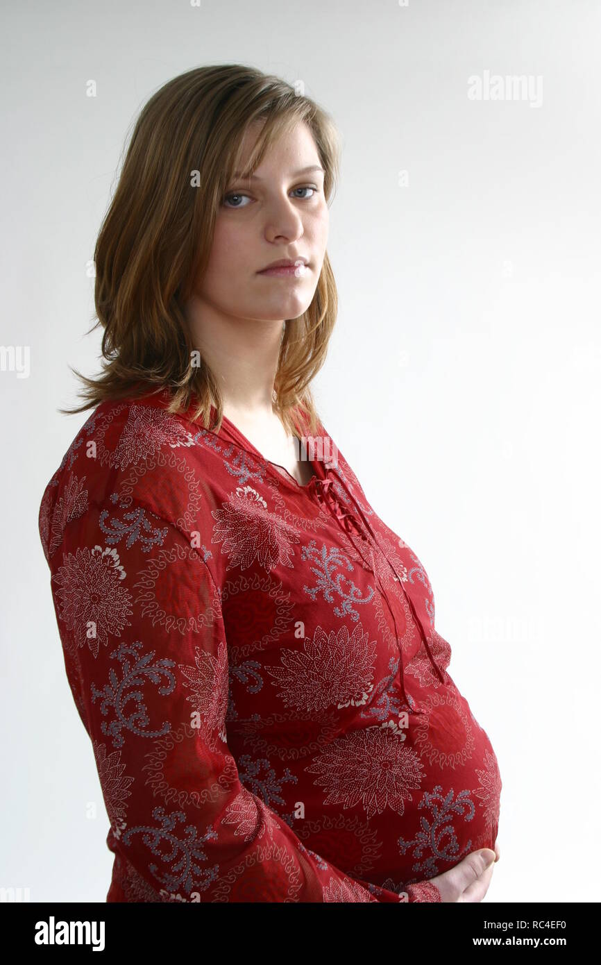 Infeliz mujer embarazada mira la cámara frente al fondo blanco. Foto de stock