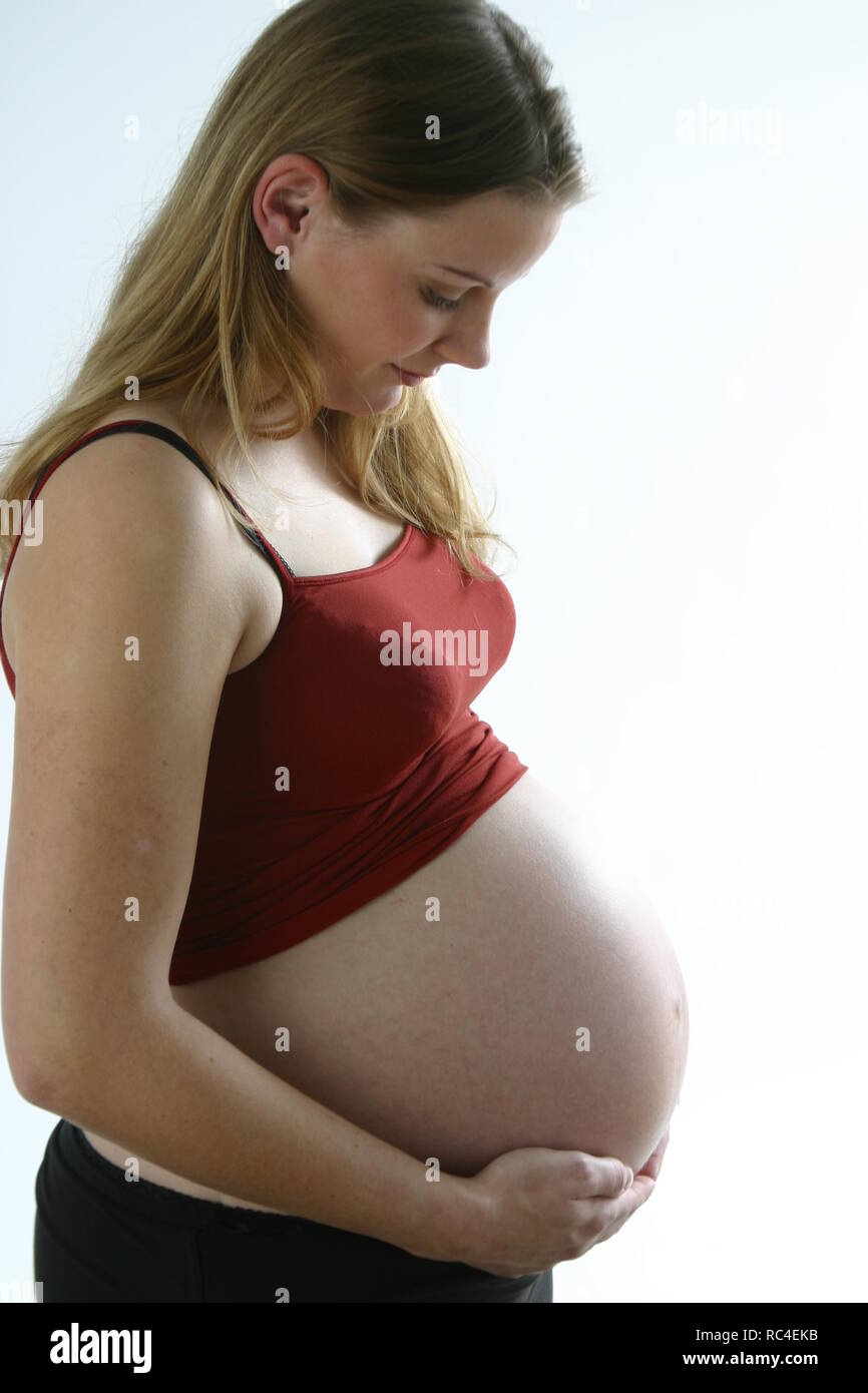 Hermosa vista lateral durante 30 mujer embarazada sostiene su vientre desnudo, tercer trimestre de embarazo. Foto de stock