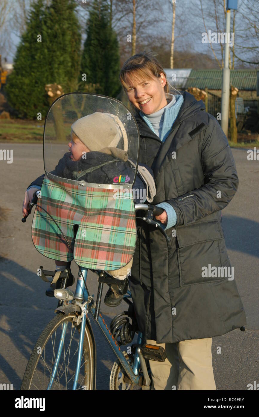Vista frontal del Cáucaso 30 feliz sobre la madre y el niño en el asiento de pie cerca de bicicleta al aire libre y feliz mirar a cámara Foto de stock
