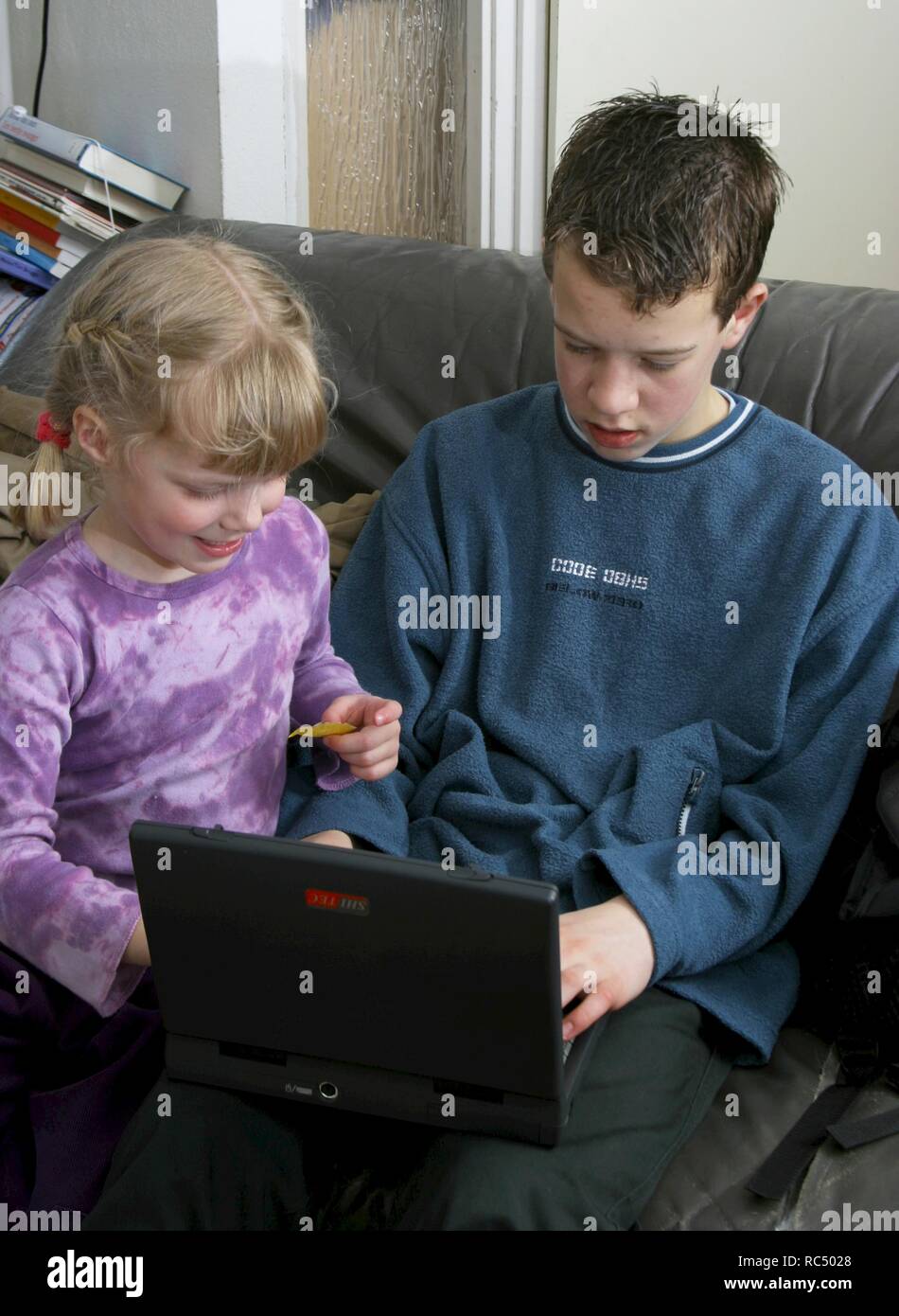 Jovencita curiosa unirse a hermano con laptop en la vuelta en casa, utilizando internet Foto de stock