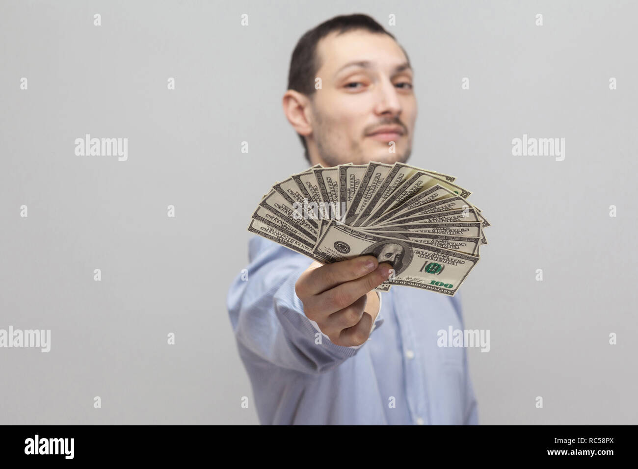 Es para usted! Retrato de satisfecho seguro atractivo adulto joven empresario en camisa azul de pie, mostrando, dándole fan de dinero. Interior, el STU Foto de stock