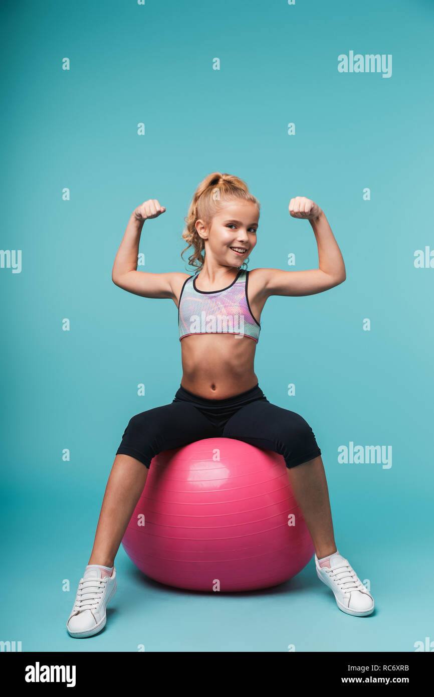 Alegre niña vistiendo ropa deportiva haciendo ejercicios con pelota fitness  aislado sobre fondo azul Fotografía de stock - Alamy