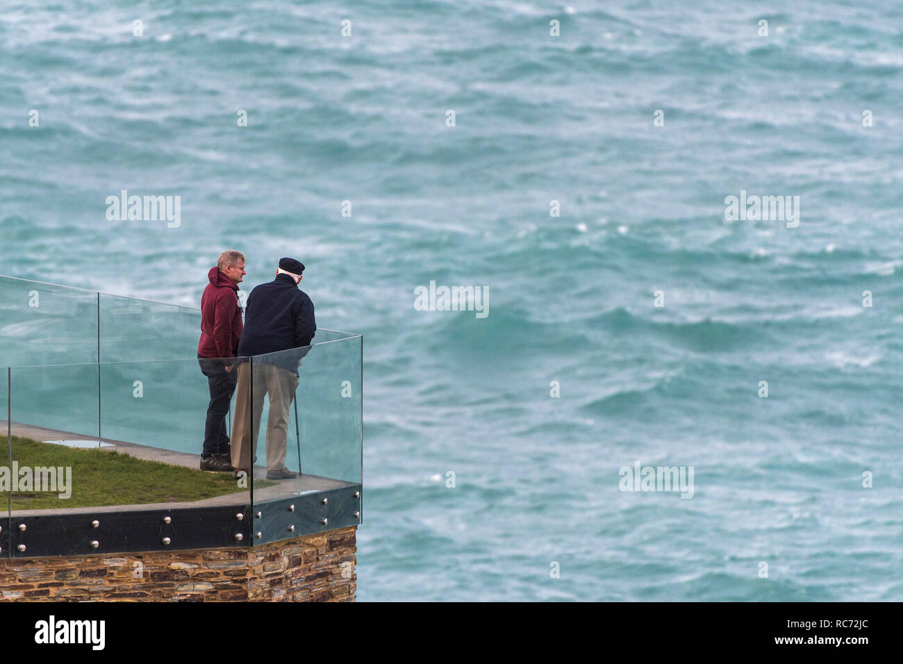 Dos hombres de pie y conversando sobre un balcón con vistas al mar. Foto de stock