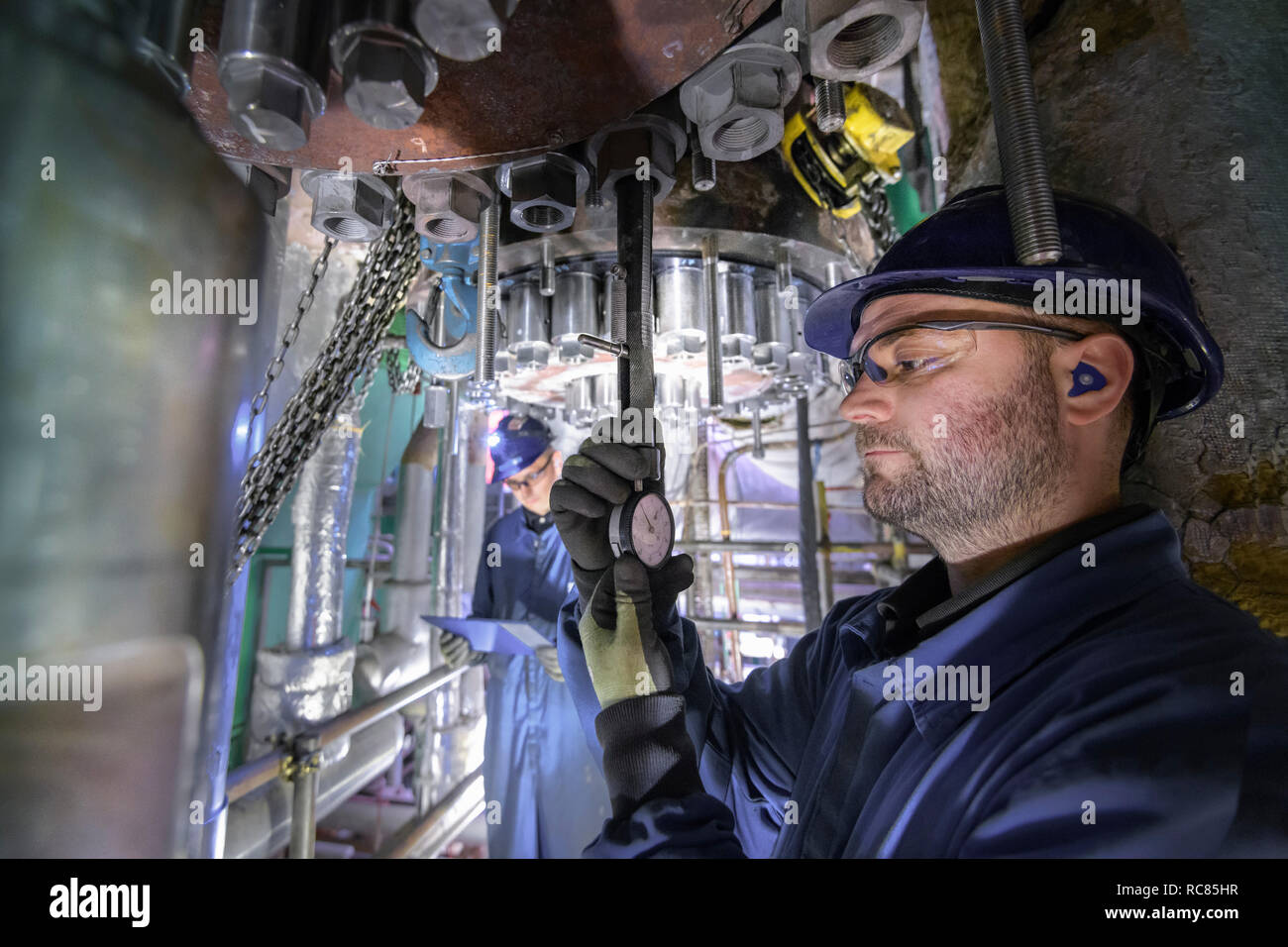 Ingeniero que trabaja en espacio reducido bajo la turbina durante la parada en la estación de energía nuclear Foto de stock