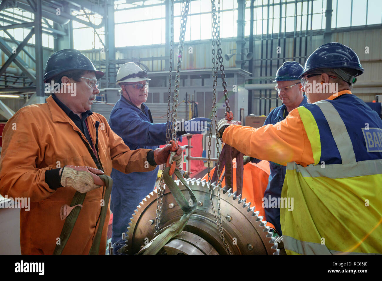 Ingenieros craning engranaje grande en su lugar en la sala de turbinas de la central nuclear Foto de stock