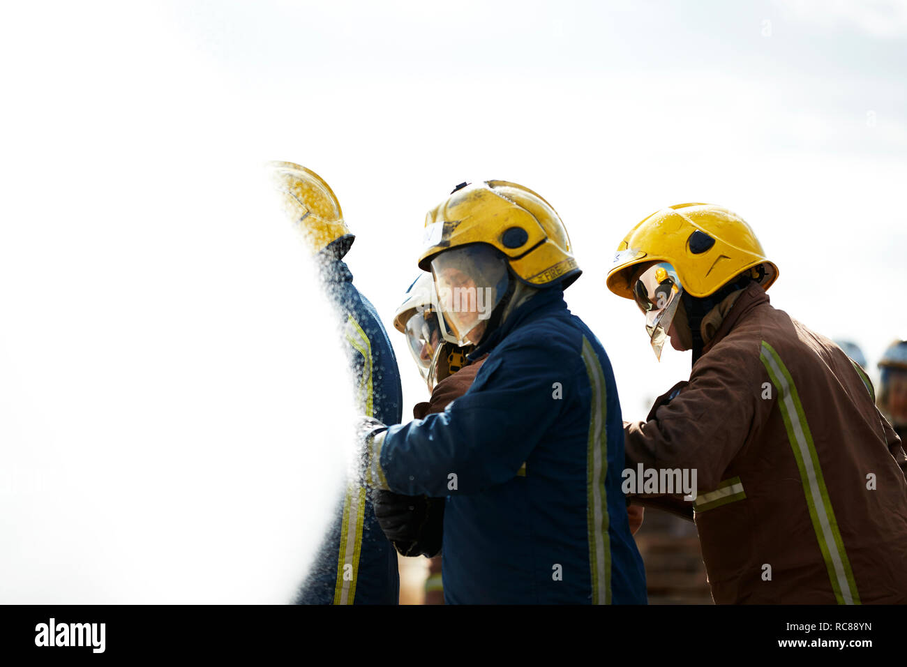 Bomberos cubiertos por pulverización de agua desde la manguera contra incendios Foto de stock