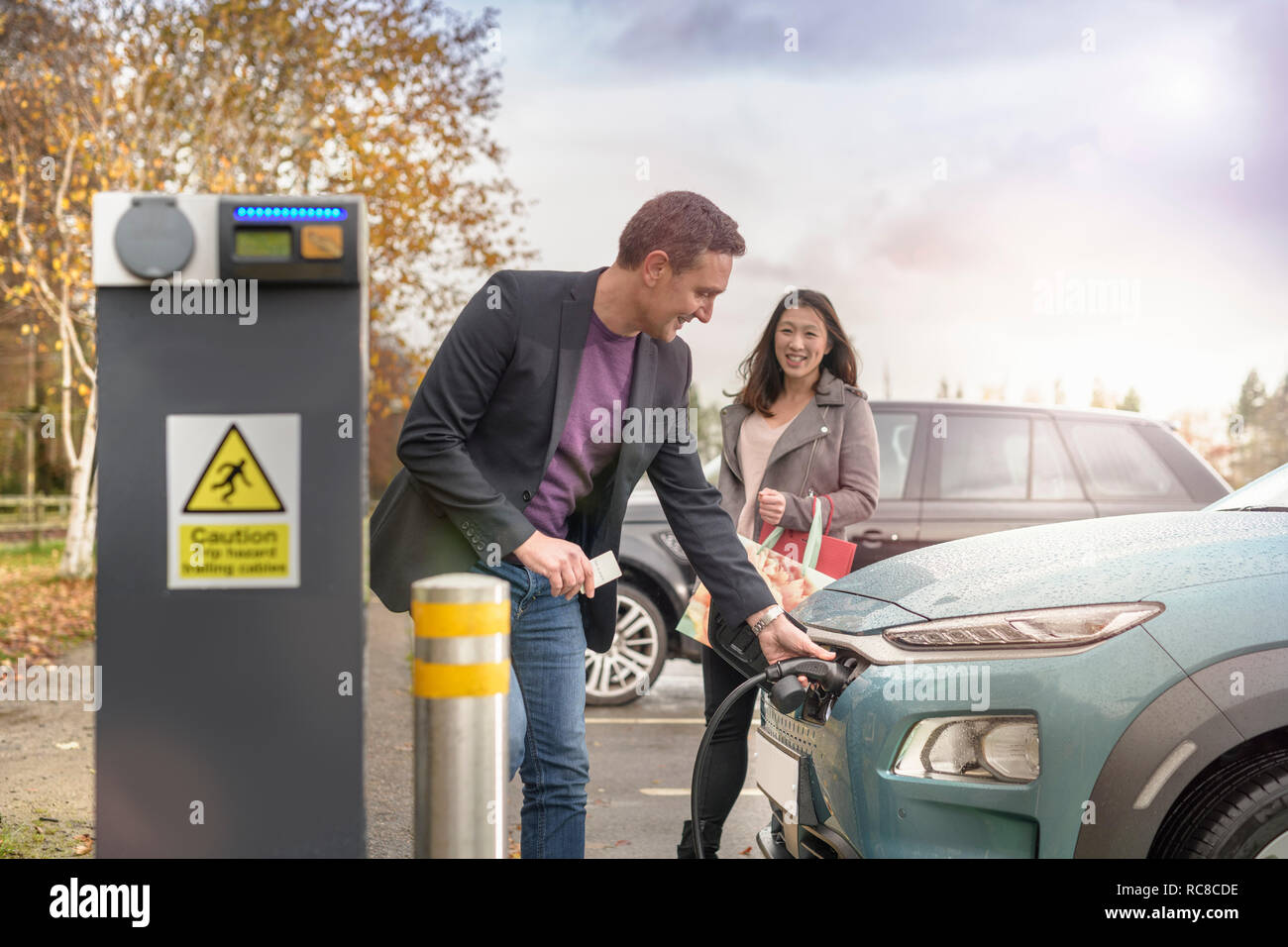 Hombre y mujer cargando un coche eléctrico en el coche cargando Park, Manchester, Reino Unido Foto de stock