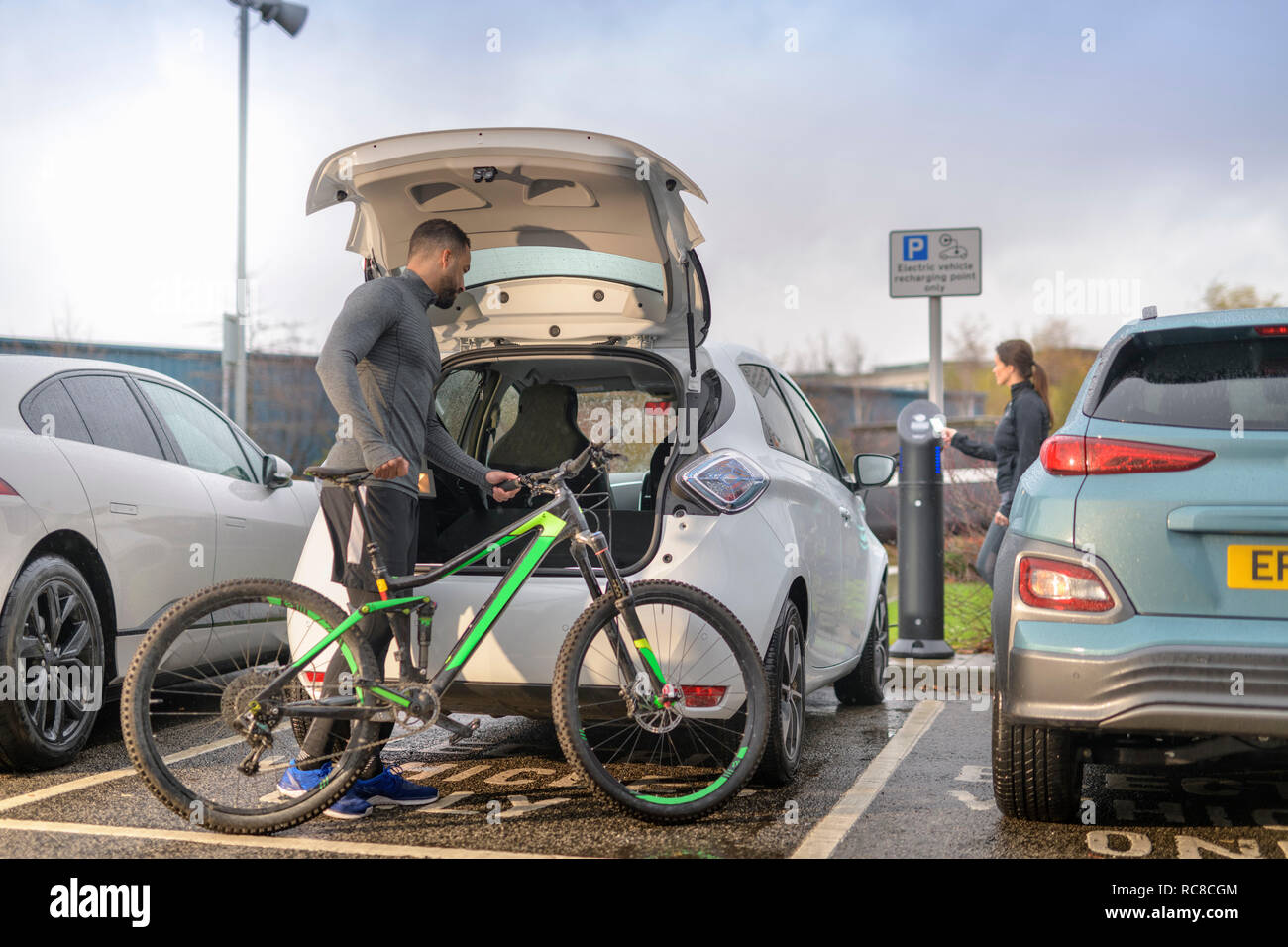 El hombre y la mujer con el mountain bike a punto de carga de coches eléctricos, Manchester, Reino Unido Foto de stock