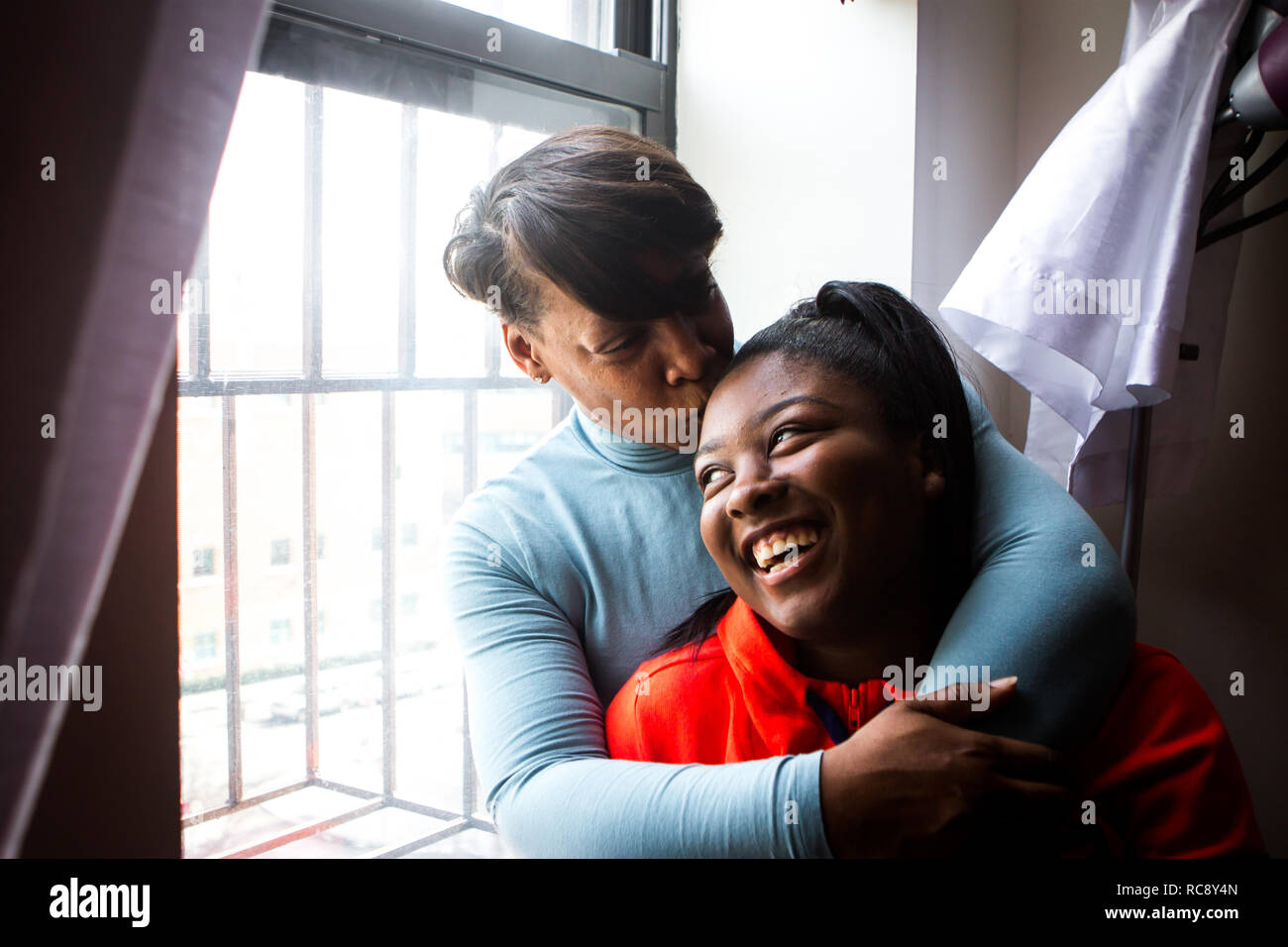 Afroamericanos madre con hija adolescente snuggle por window Foto de stock