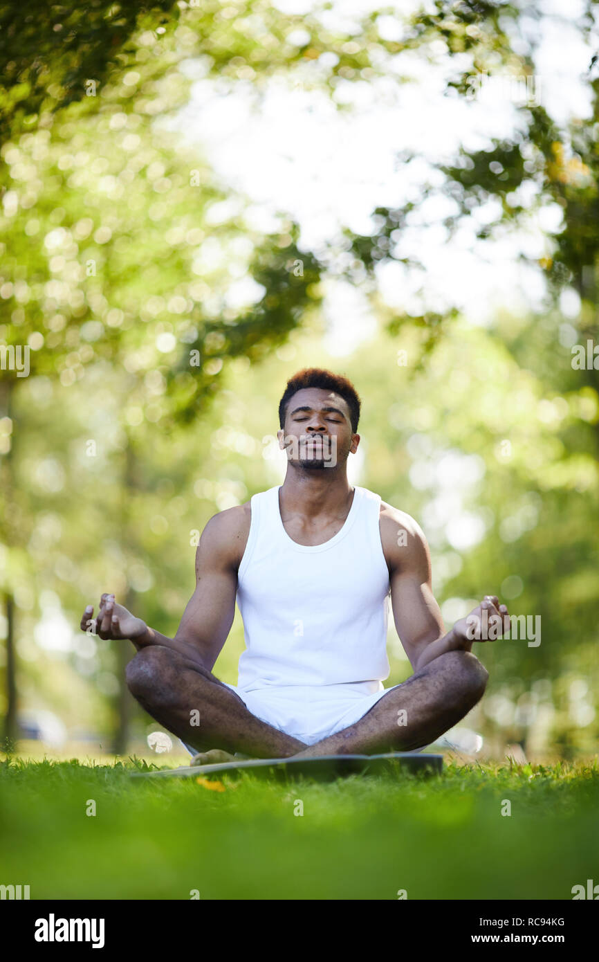Grave hombre negro con las piernas cruzadas meditando en estacionamiento Foto de stock