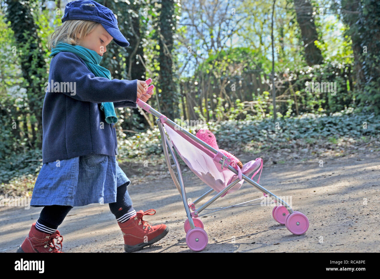 El Kleines Mädchen schiebt Puppenbuggy, 2 Jahre alt | niña mete cochecito de muñeca Foto de stock