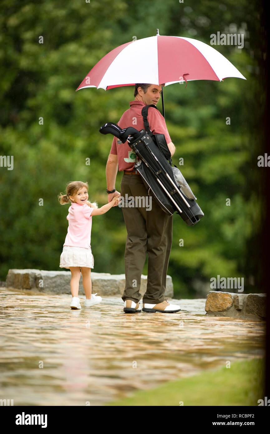 Muchacha con padre en campo de golf bajo la lluvia Foto de stock