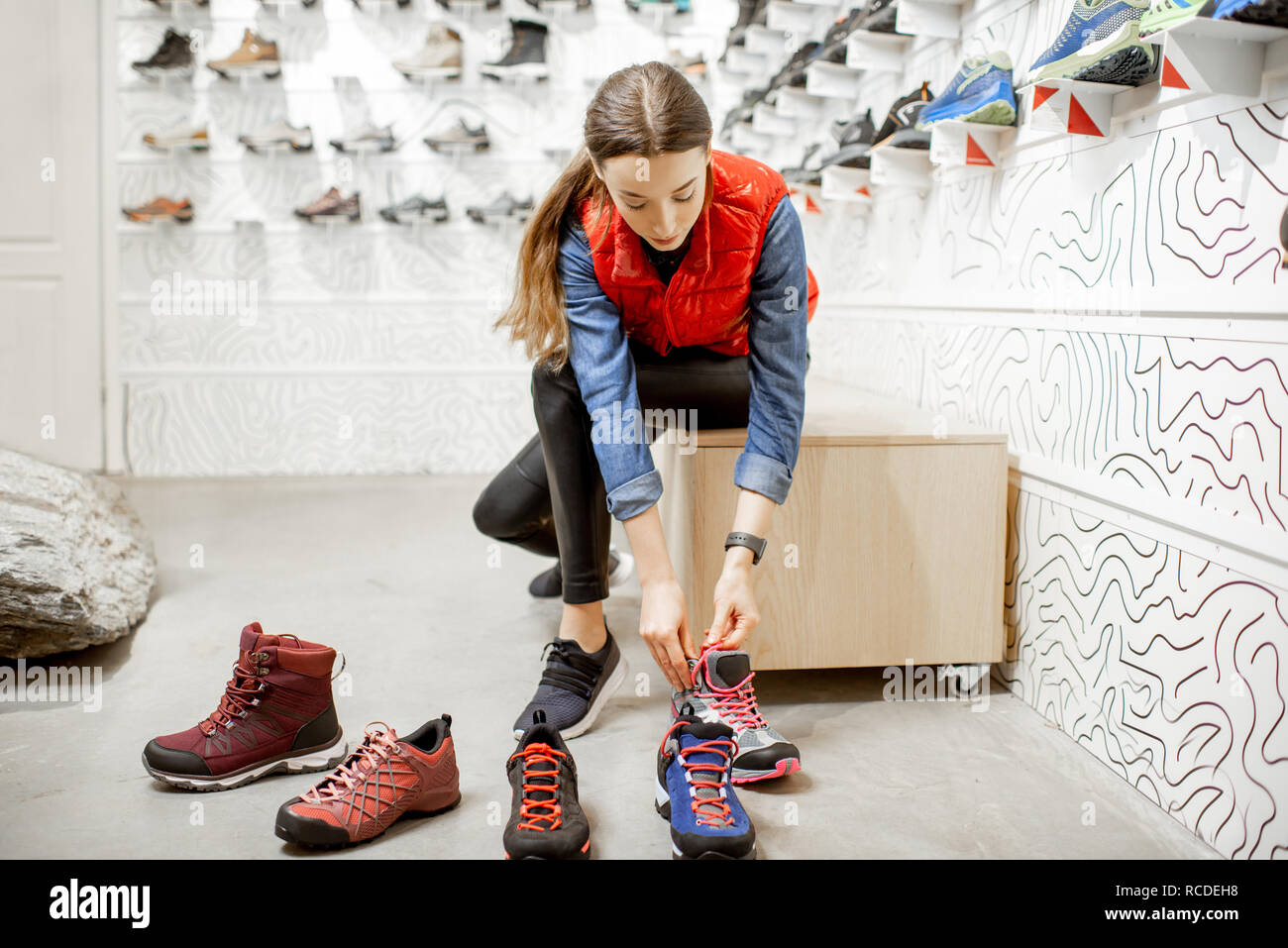 Mujer tratando de zapatos para caminatas sentado en la sala de montaje de  la moderna tienda de deportes Fotografía de stock - Alamy