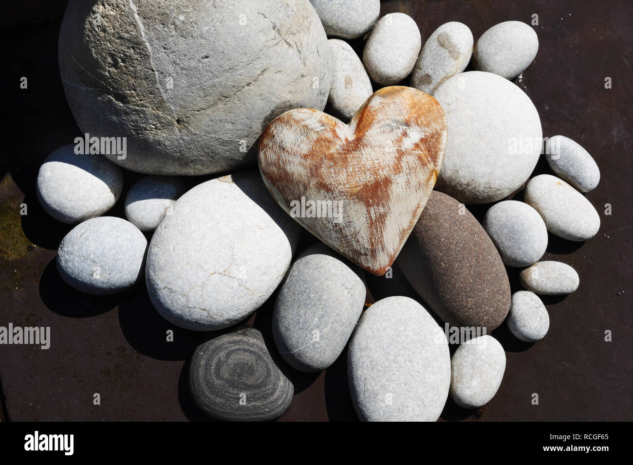 Pintado de blanco corazón de madera desgastada agrupados con guijarros de playa como decoración de jardines. Foto de stock