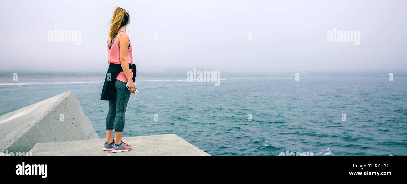 Mujer joven en bloque de cemento mirando el mar Foto de stock