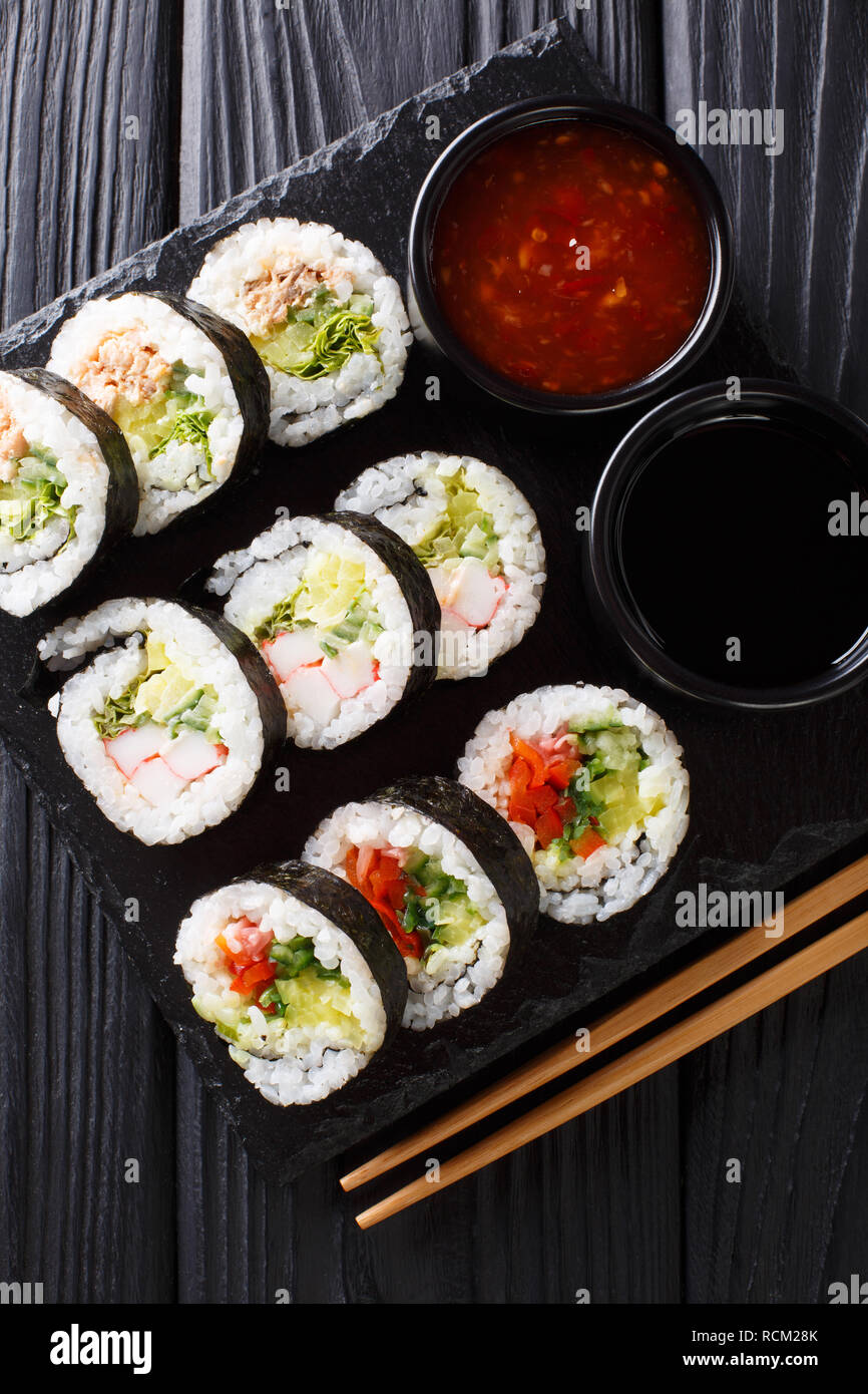 Futomaki rollos con varios rellenos son servidos con salsas de cerca en una placa de pizarra sobre la mesa. Vista superior de la vertical desde arriba Foto de stock