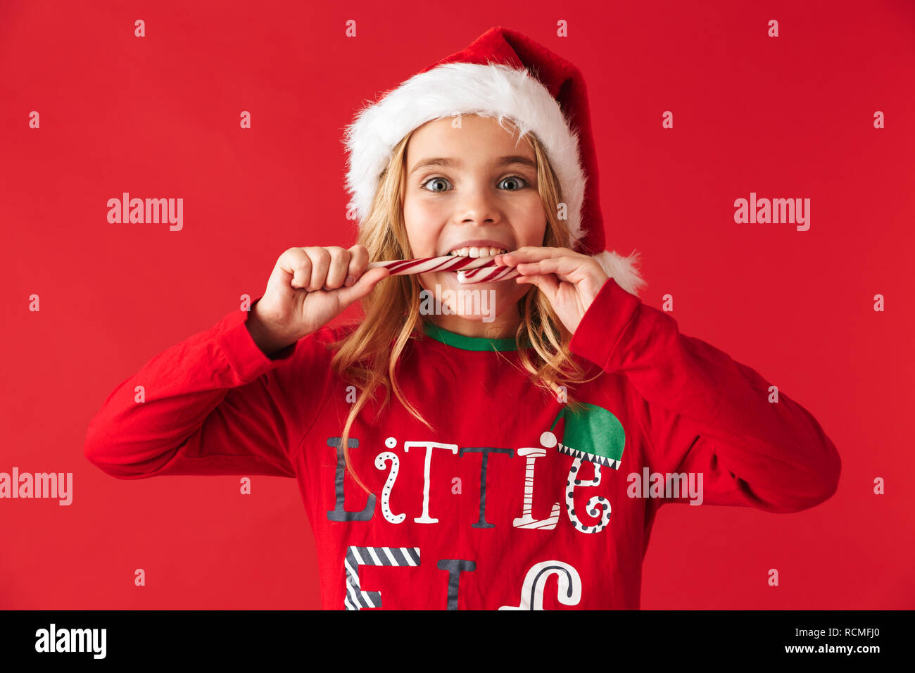 Alegre niña vestidos de traje de Navidad que se encuentran aisladas sobre  fondo rojo, comer dulces navideños dulces de cono Fotografía de stock -  Alamy
