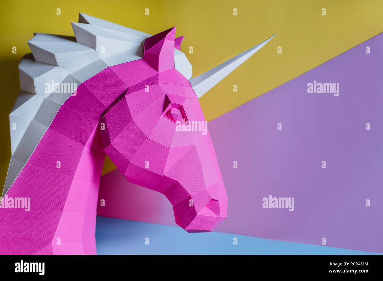 Cabeza de unicornio de papel sobre un fondo coloreado. Geometría, brillante y colores pastel. Foto de stock