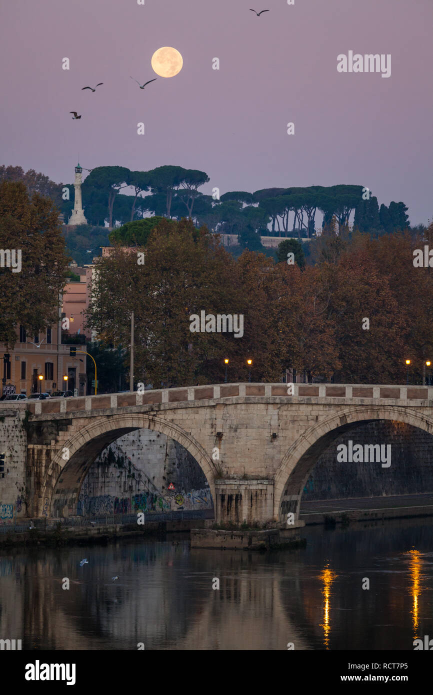 Amanece sobre Roma con una luna llena que adornan el Tíber, el Ponte Sisto y el faro del Janículo en la distancia. Foto de stock