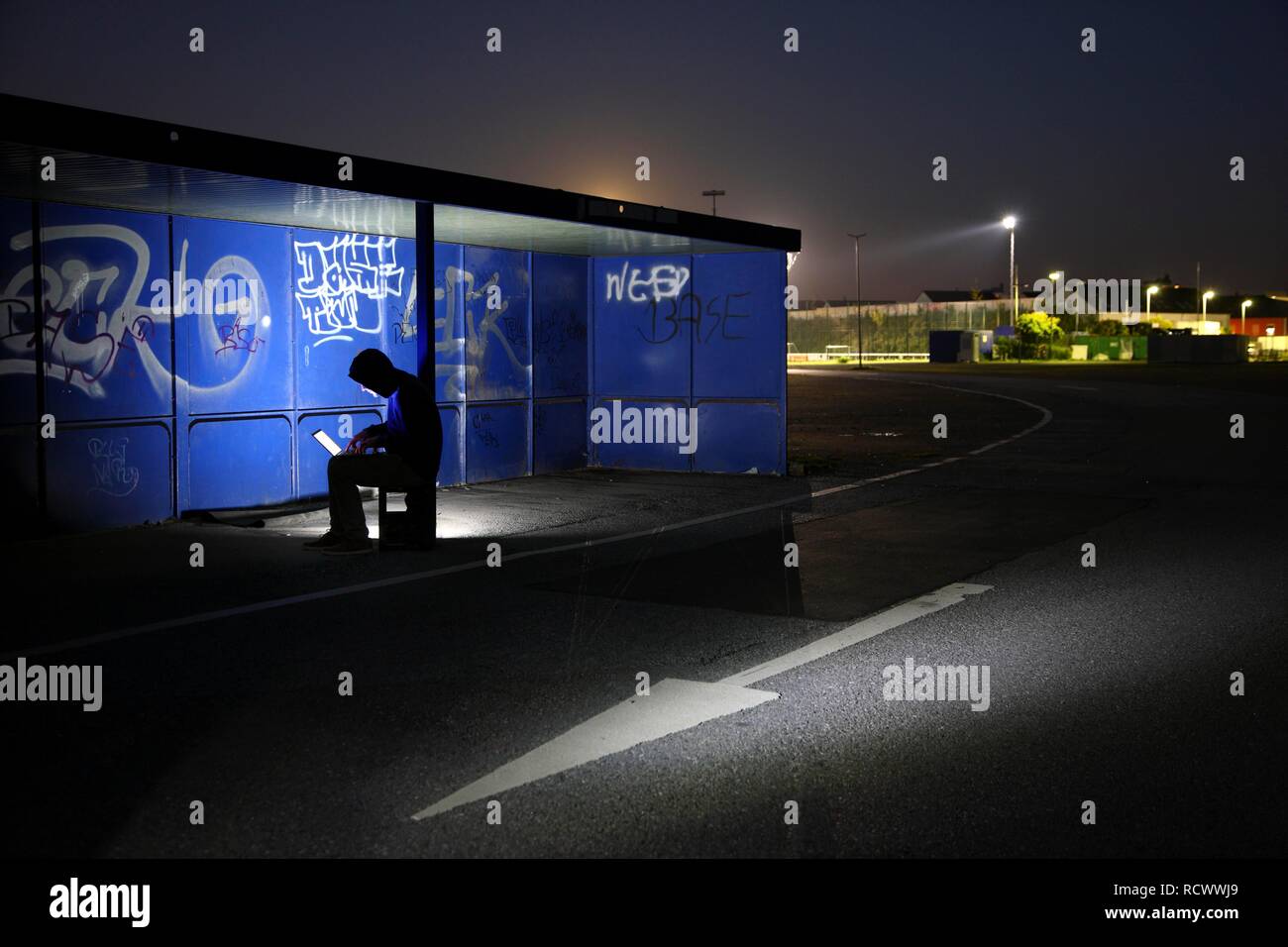 El hombre navegando en un ordenador portátil en una parada de autobús por la noche, la imagen simbólica de la piratería informática, los delitos informáticos, cibercriminalidad Foto de stock