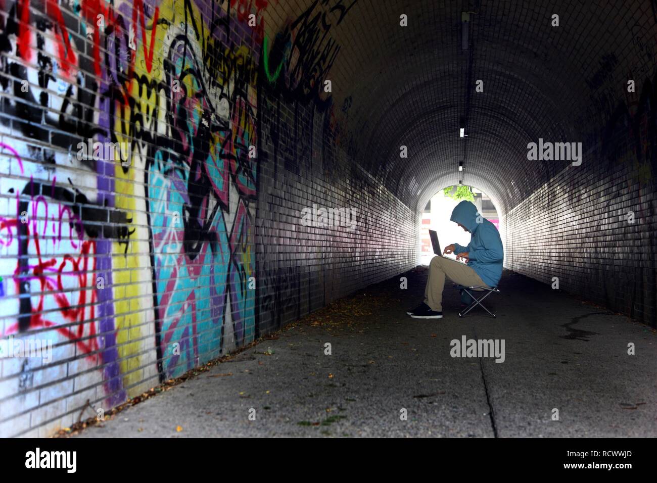 El hombre navegando en un ordenador portátil en un túnel peatonal, imagen simbólica para la piratería informática, los delitos informáticos, cibercriminalidad Foto de stock