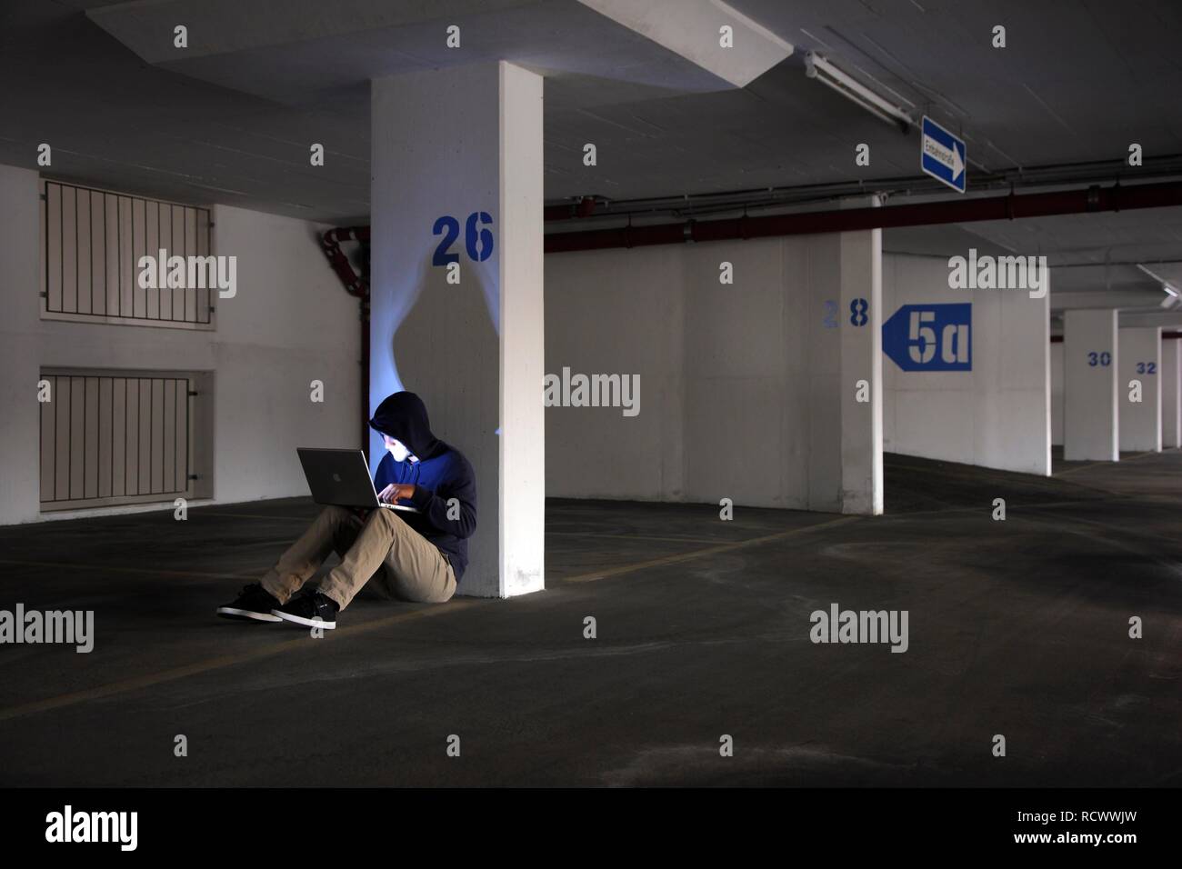 El hombre navegando en un ordenador portátil en un vacío estacionamiento de varios pisos, imagen simbólica para la piratería informática y delito informático Foto de stock