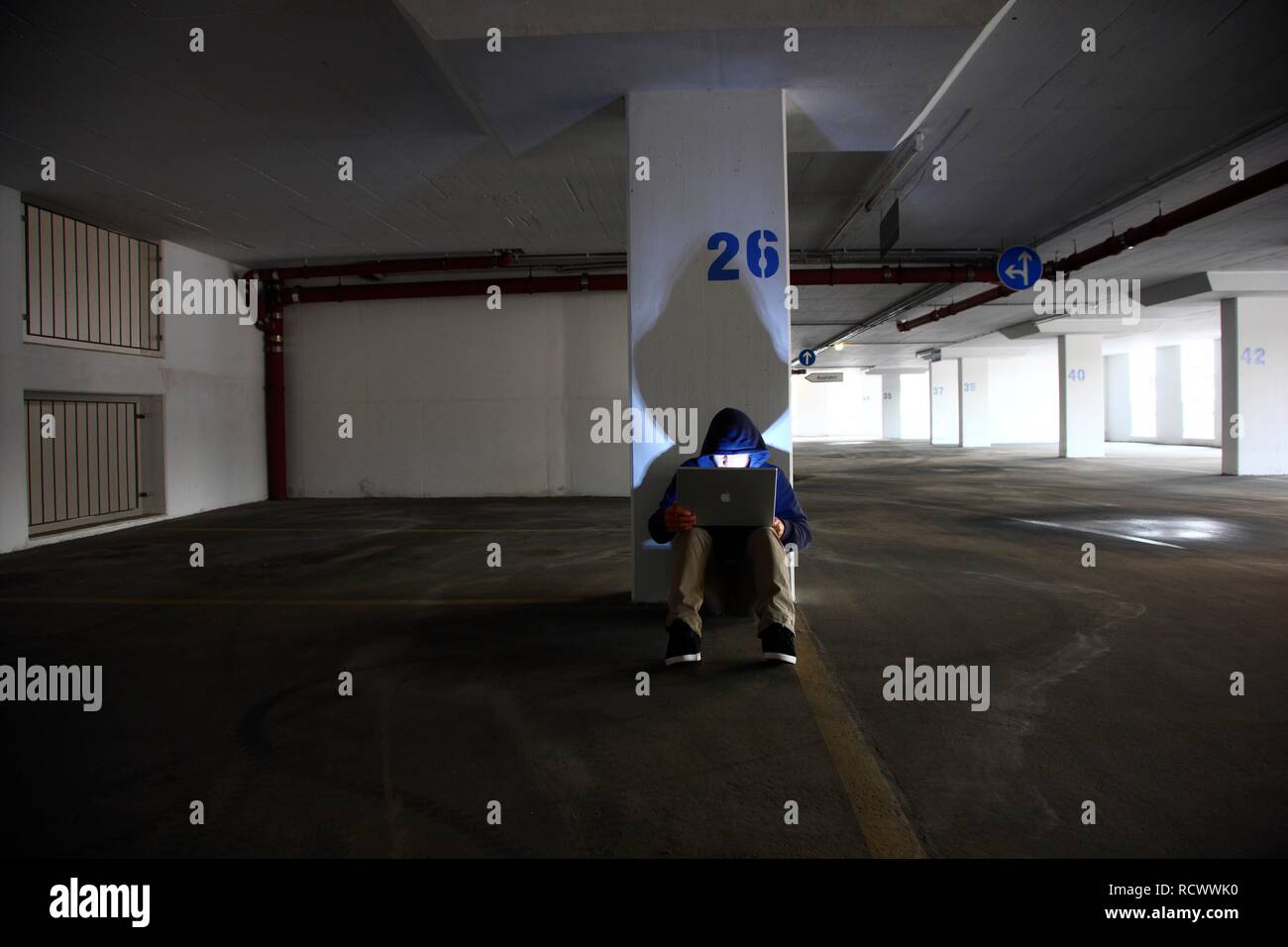 El hombre navegando en un ordenador portátil en un vacío estacionamiento de varios pisos, imagen simbólica para la piratería informática y delito informático Foto de stock