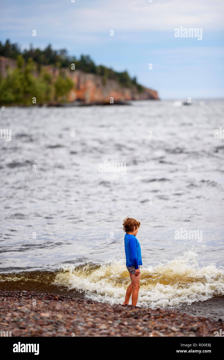 Niño de pie al borde del agua, mirando al mar, Estados Unidos Foto de stock