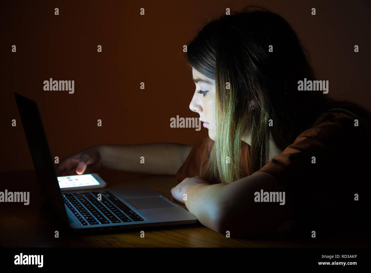 Una bonita adolescente utilizando su ordenador portátil y teléfono móvil durante la noche. Foto de stock