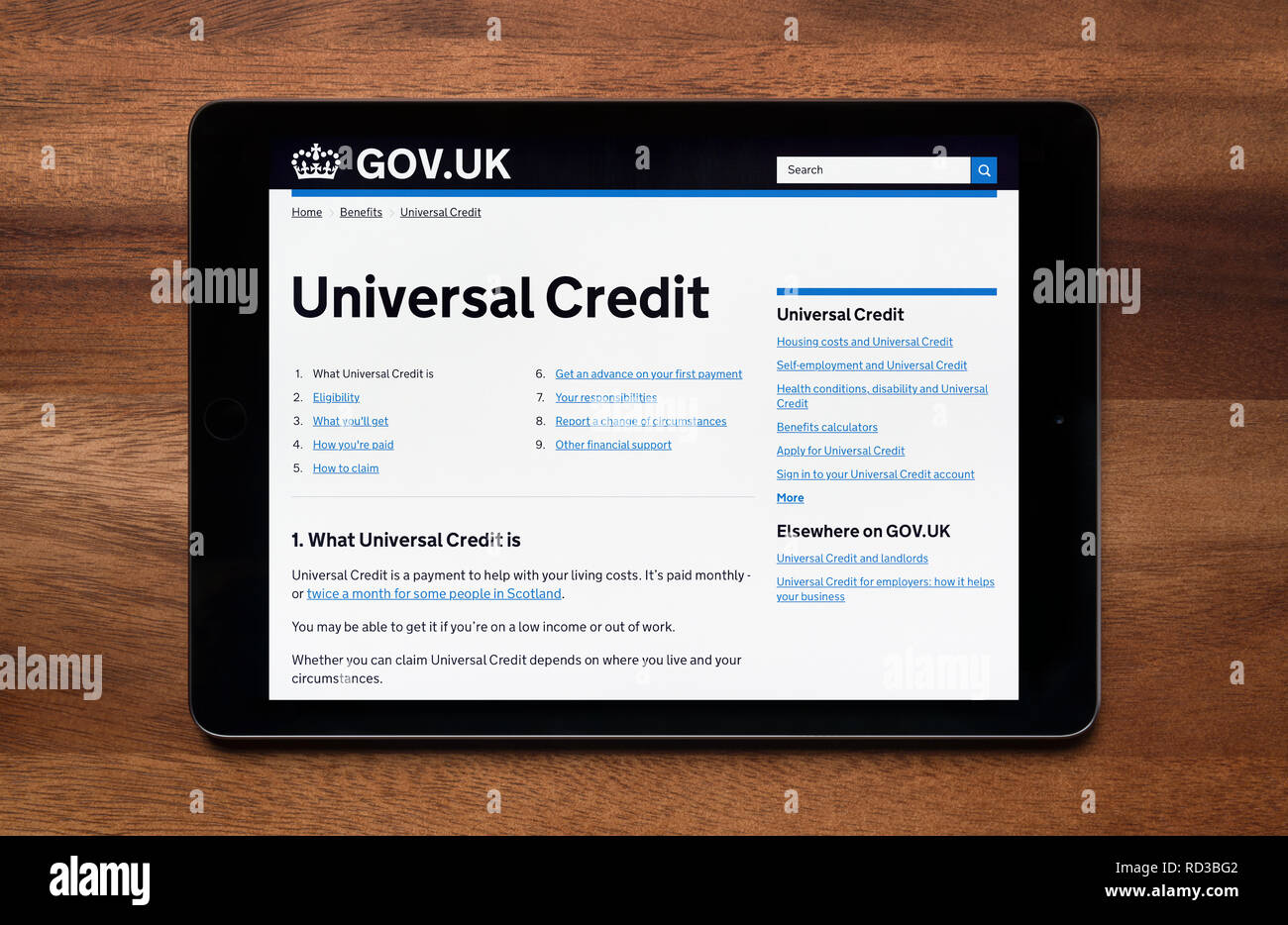 El sitio web de la sección de crédito universal de la gov.uk sitio web es visto en un iPad, que descansa sobre una mesa de madera (uso Editorial solamente). Foto de stock