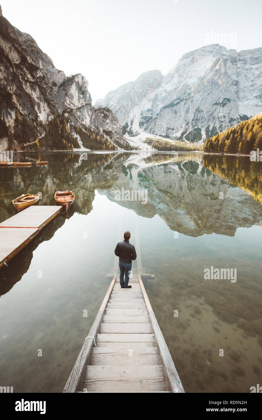 Hermosa vista de un joven parado sobre escaleras de madera viendo el amanecer en el famoso Lago di Braies los Dolomitas, Tirol del Sur, Italia Foto de stock