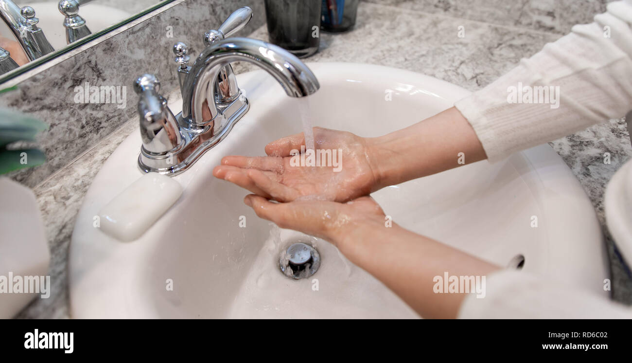 Los jóvenes caucásicos manos femeninas Lathering barra blanca jabón para lavar a mano y artículos de higiene personal y, a continuación, lavado de manos bajo fregadero agua en un baño limpio. Foto de stock