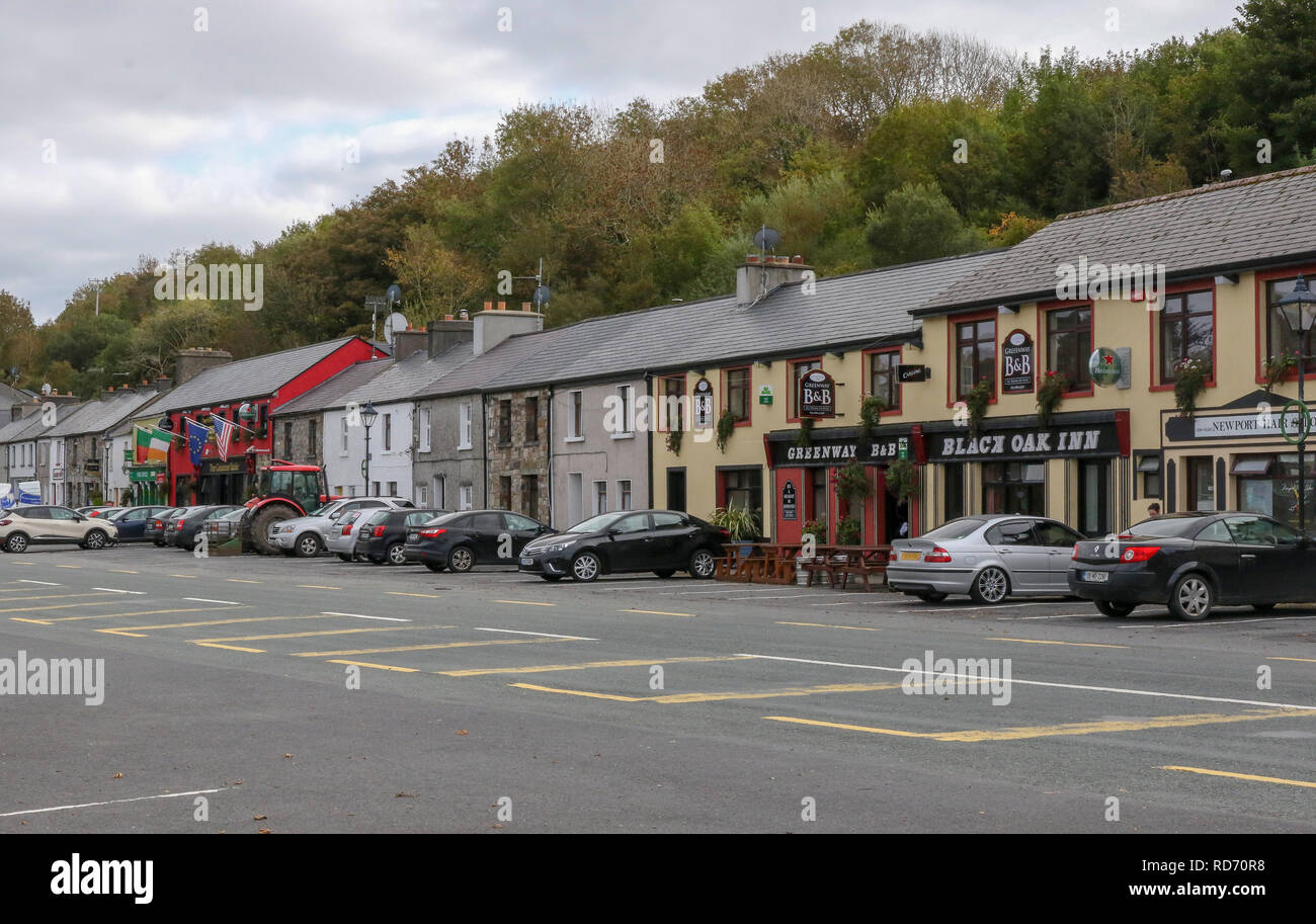 Los coches aparcados en la carretera fuera de edificios y casas en Irlanda en Newport, en el condado de Mayo, Irlanda. Foto de stock