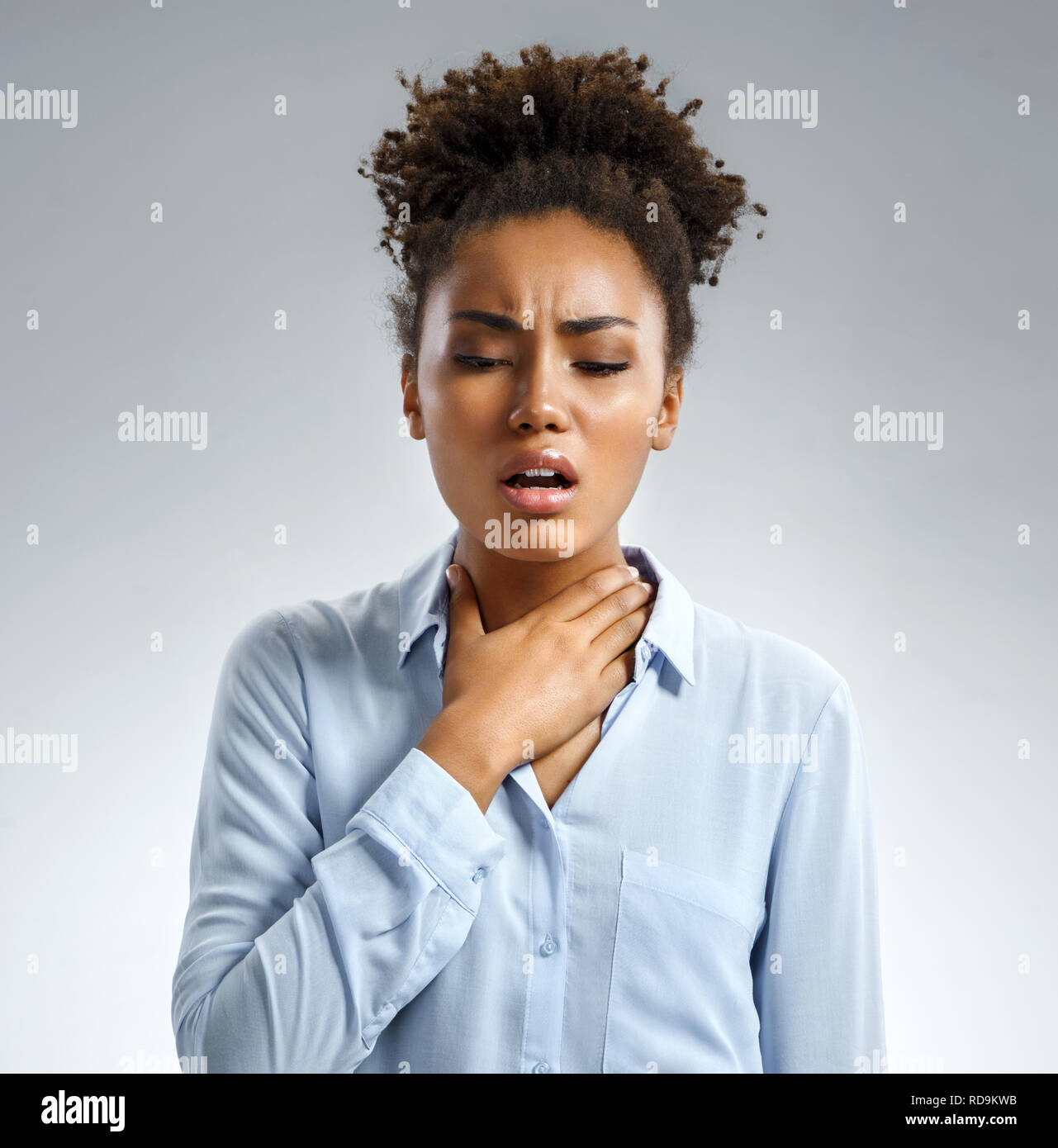 El dolor de garganta. Mujer sosteniendo su garganta inflamada. Foto de afroamericana en camisa azul sobre fondo gris. Concepto médico Foto de stock
