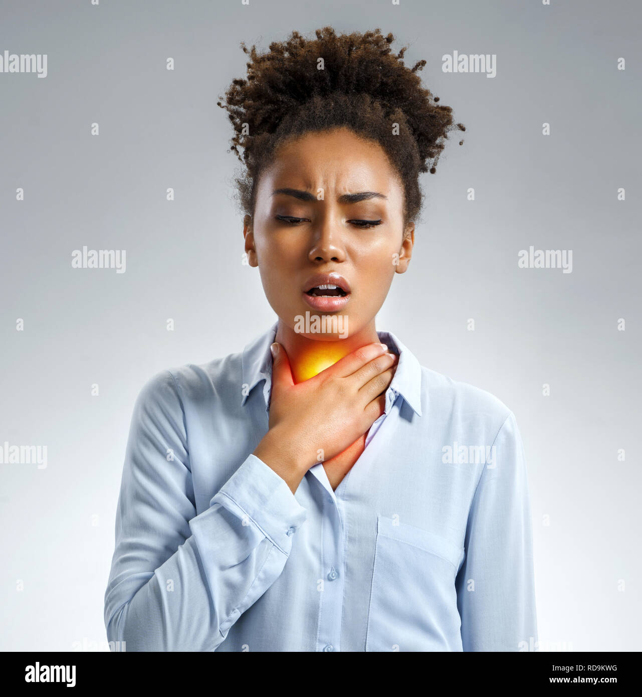 El dolor de garganta. Mujer sosteniendo su garganta inflamada. Foto de afroamericana en camisa azul sobre fondo gris. Concepto médico Foto de stock