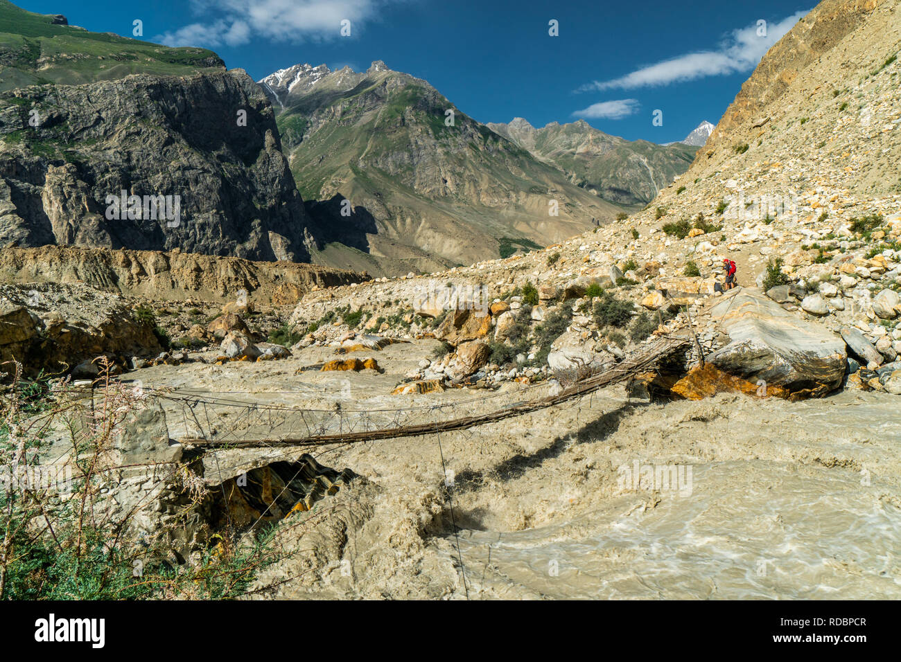 Peligroso cruzar el río en Puente frágil a lo largo de un río salvaje de las montañas Karakoram en Pakistán Foto de stock