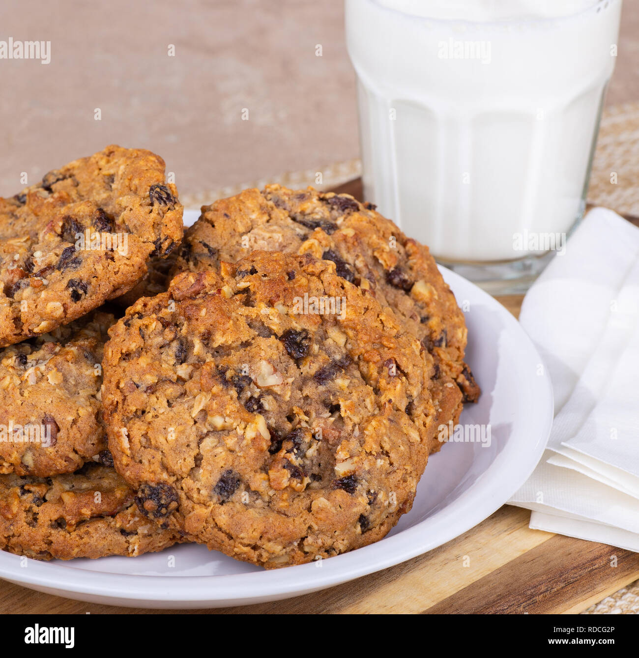 Primer plano de un montón de avena tuerca raisin cookies en una placa con un vaso de leche en segundo plano. Foto de stock
