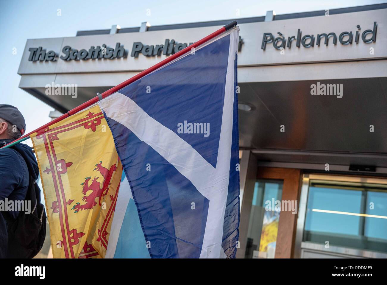 Un hombre es visto sosteniendo las banderas a la entrada del edificio del Parlamento Escocés. Los manifestantes se reunieron frente al edificio del Parlamento Escocés en Edimburgo para protestar Brexit y empujar a un segundo referéndum de independencia. Foto de stock