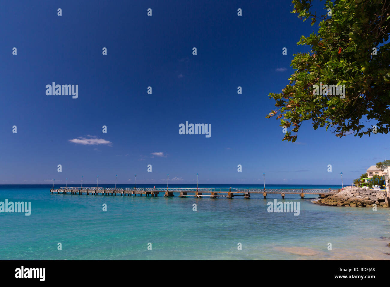 El muelle en la playa de Mullins, Barbados se estira en un mar turquesa, bajo un cielo azul claro. Foto de stock