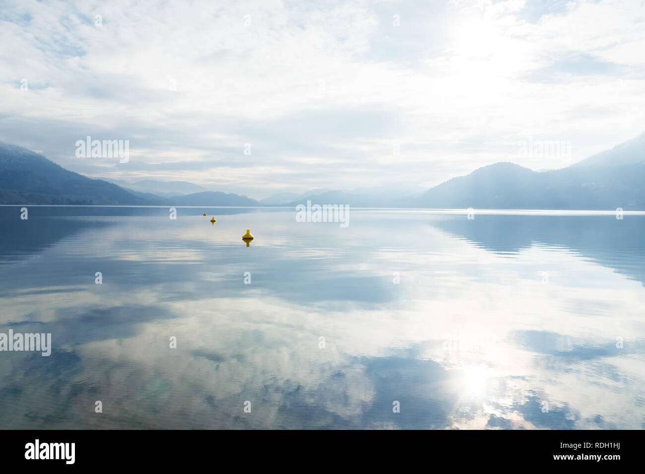Nubes, niebla, sol y montañas reflejadas en el lago en calma Foto de stock