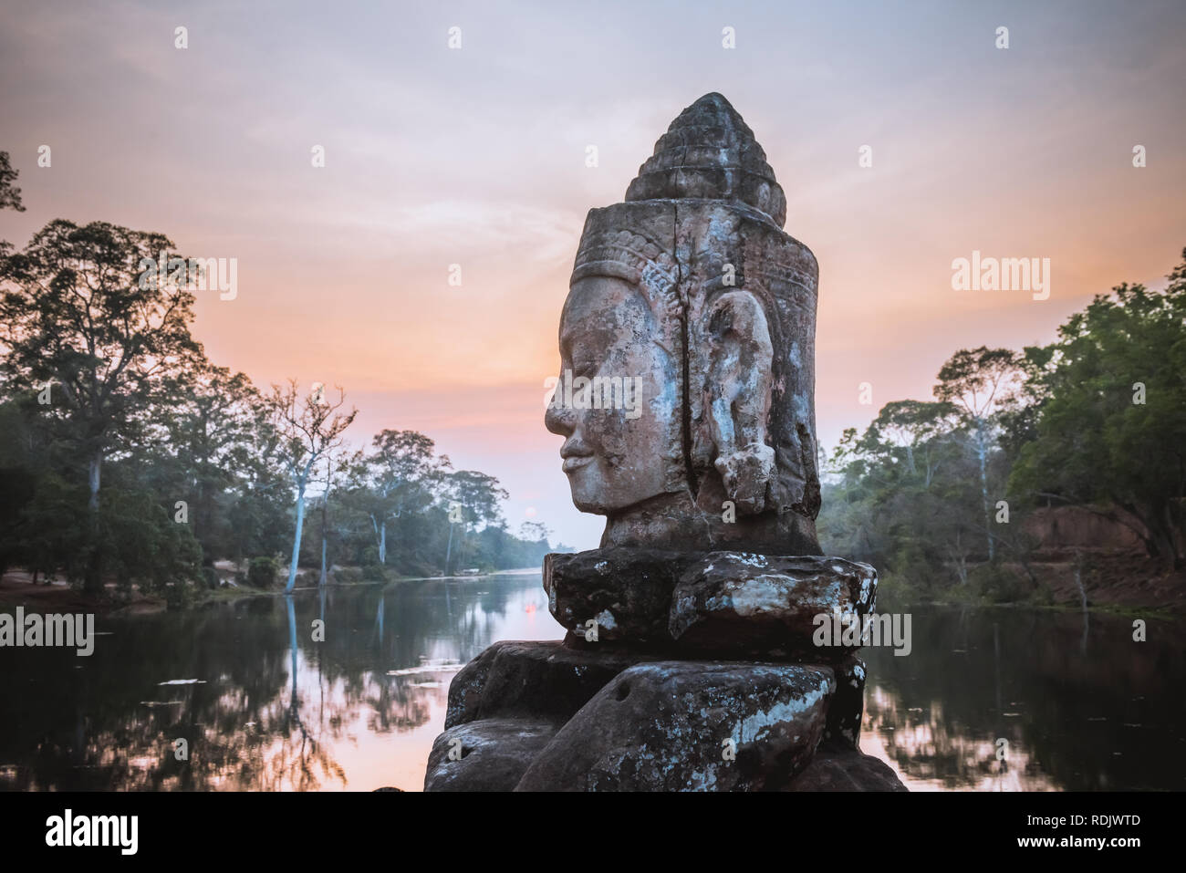 Asura de piedra sobre la calzada cerca de la puerta sur de Angkor en Siem Reap, Camboya. Hermoso atardecer en antiguo foso en segundo plano. Angkor Thom es una población Foto de stock