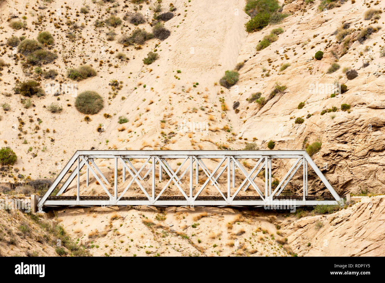 Un puente sobre el ferrocarril Transandine en desuso está siendo devorada por la arena y la grava erosionados desde la ladera de la colina. Esta sección se encuentra en Argentina. Foto de stock
