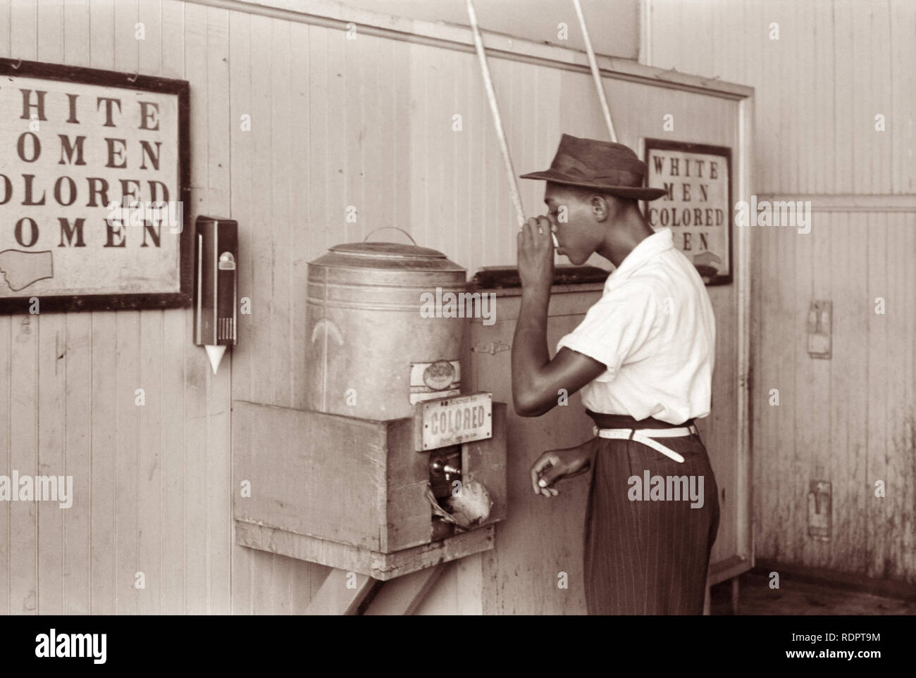 Hombre Negro bebiendo en un 'Color' en un enfriador de agua de la ciudad de Oklahoma, Oklahoma terminal de tranvía en julio de 1939. Foto de stock