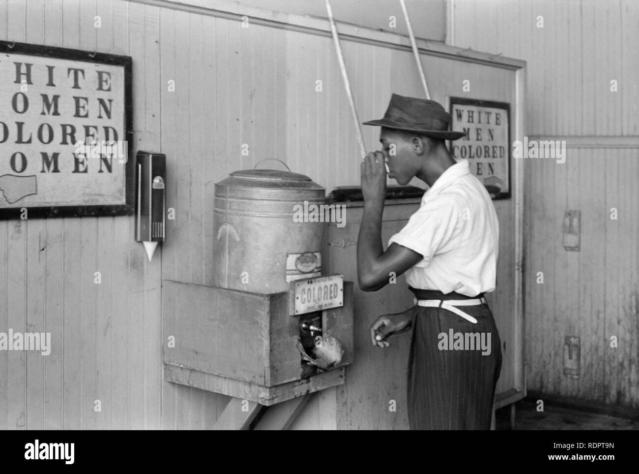 Hombre Negro bebiendo en un 'Color' en un enfriador de agua de la ciudad de Oklahoma, Oklahoma terminal de tranvía en julio de 1939. Foto de stock