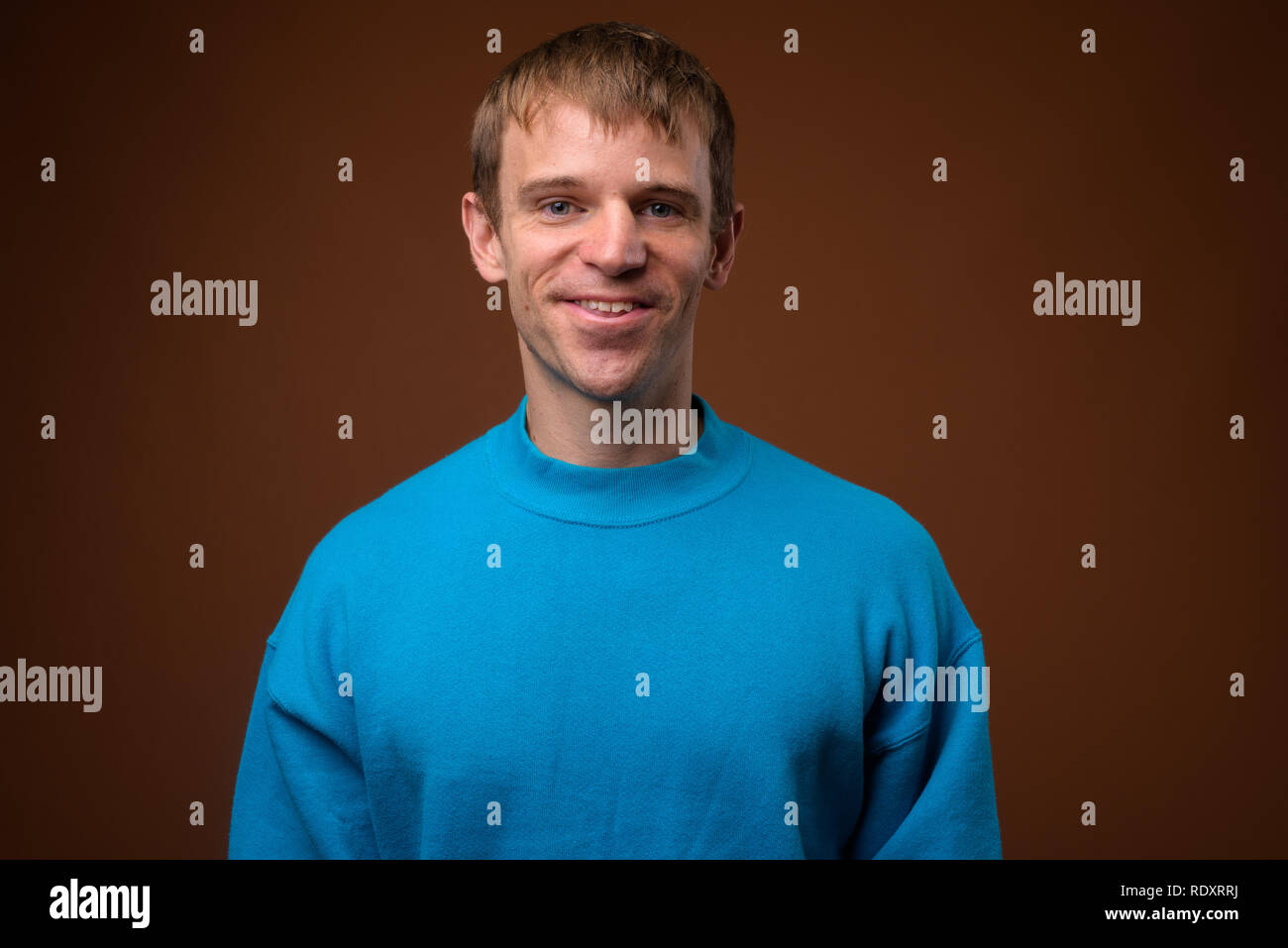 Hombre que llevaba un suéter azul contra el fondo marrón Foto de stock