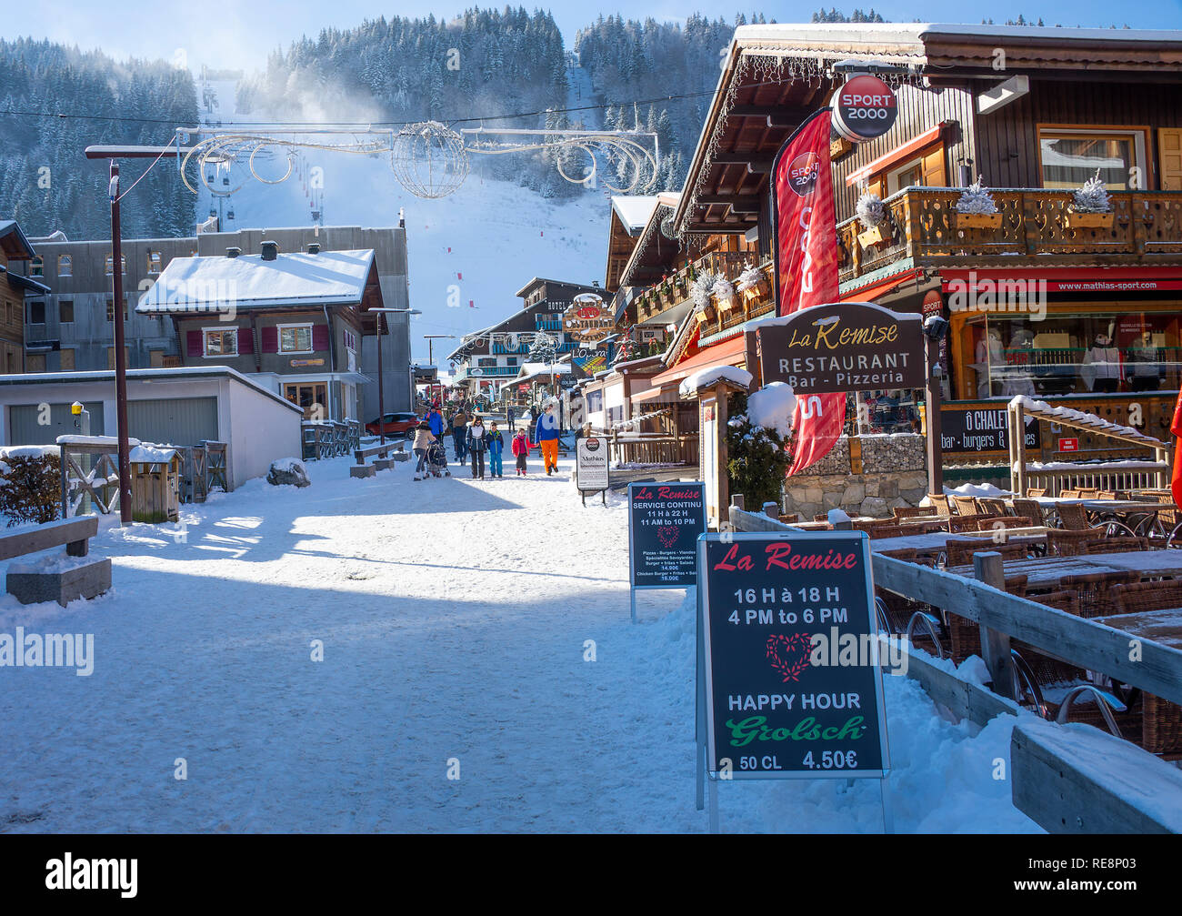 Tiendas pintorescas y restaurantes con pistas de esquí detrás y cubiertas de nieve en la calle Morzine Haute Savoie Portes du Soleil Francia Foto de stock