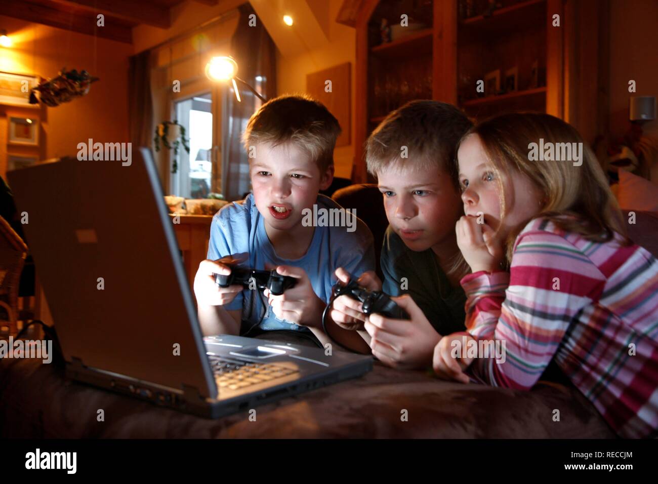 Hermanos, 7, 11, 13 años de edad, con ordenador portátil en el salón, jugando a un videojuego de carreras de coches Foto de stock