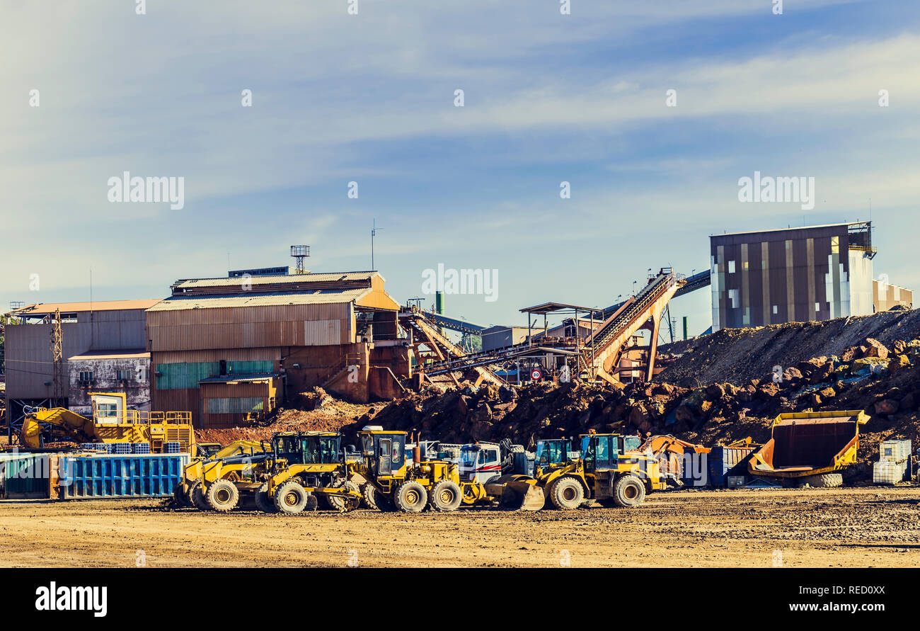 Las cargadoras de ruedas y otras máquinas para minería aparcado junto a los antiguos edificios, con el cielo azul con nubes en el fondo Foto de stock