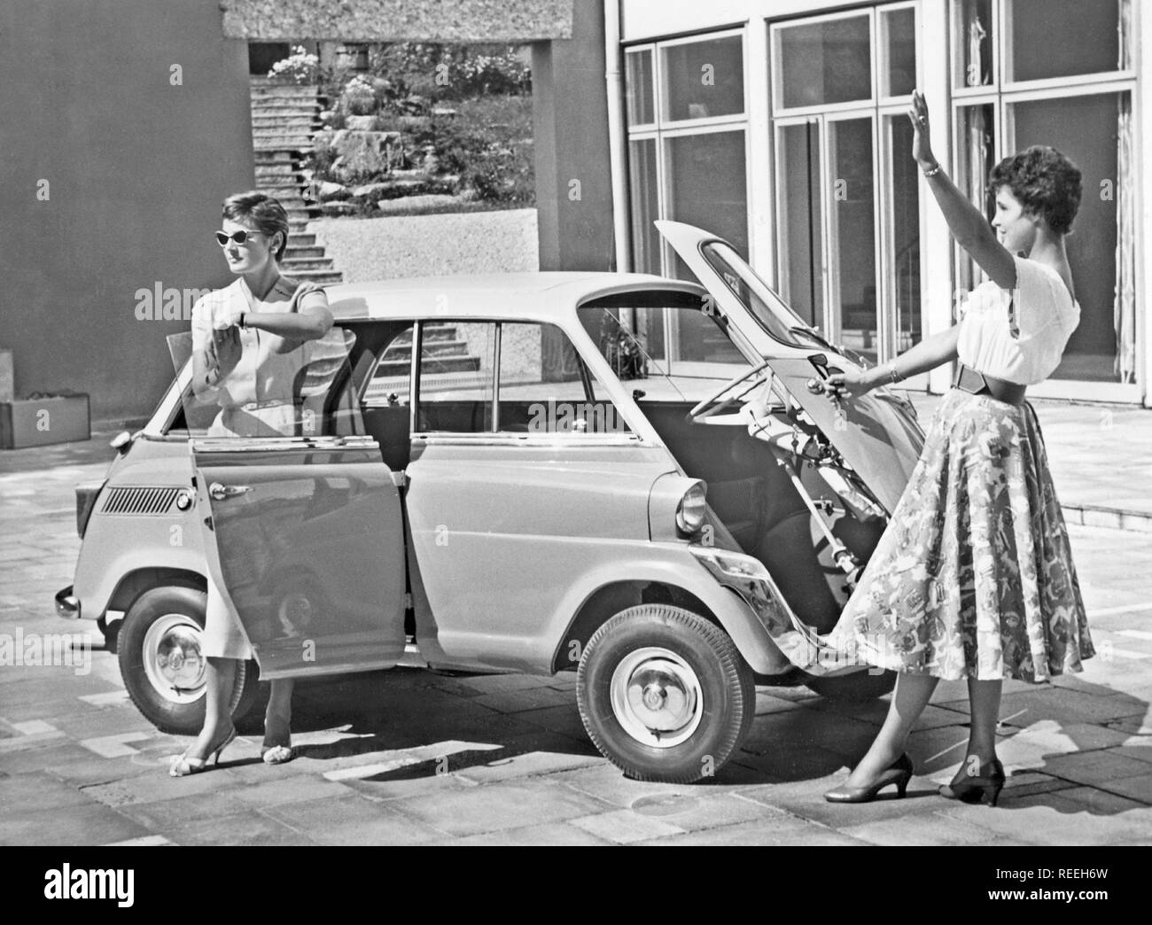 La conducción en el decenio de 1950. Dos mujeres jóvenes está de pie junto a un coche modelo BMW 600. Un micro modelo de coche con la puerta delantera justo delante. 1958 Foto de stock